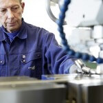 Älterer Mann im Fokus hinter einer Maschine die nur schemenhaft zu erkennen ist