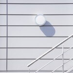 Runde Lampe an der Außenwand eines Gebäudes. Treppenstufen aus Stahl seitlich am Gebäude.