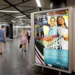 Plakate um eine Säule und verschwommene Personen beim Gehen in der B-Ebene einer Haltestelle