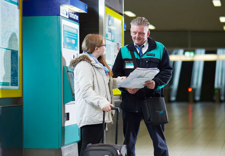Mitarbeiter der VGF steht mit junger Frau vor einem Fahrkartenautomaten und hält einen Linienfahrplan in der Hand