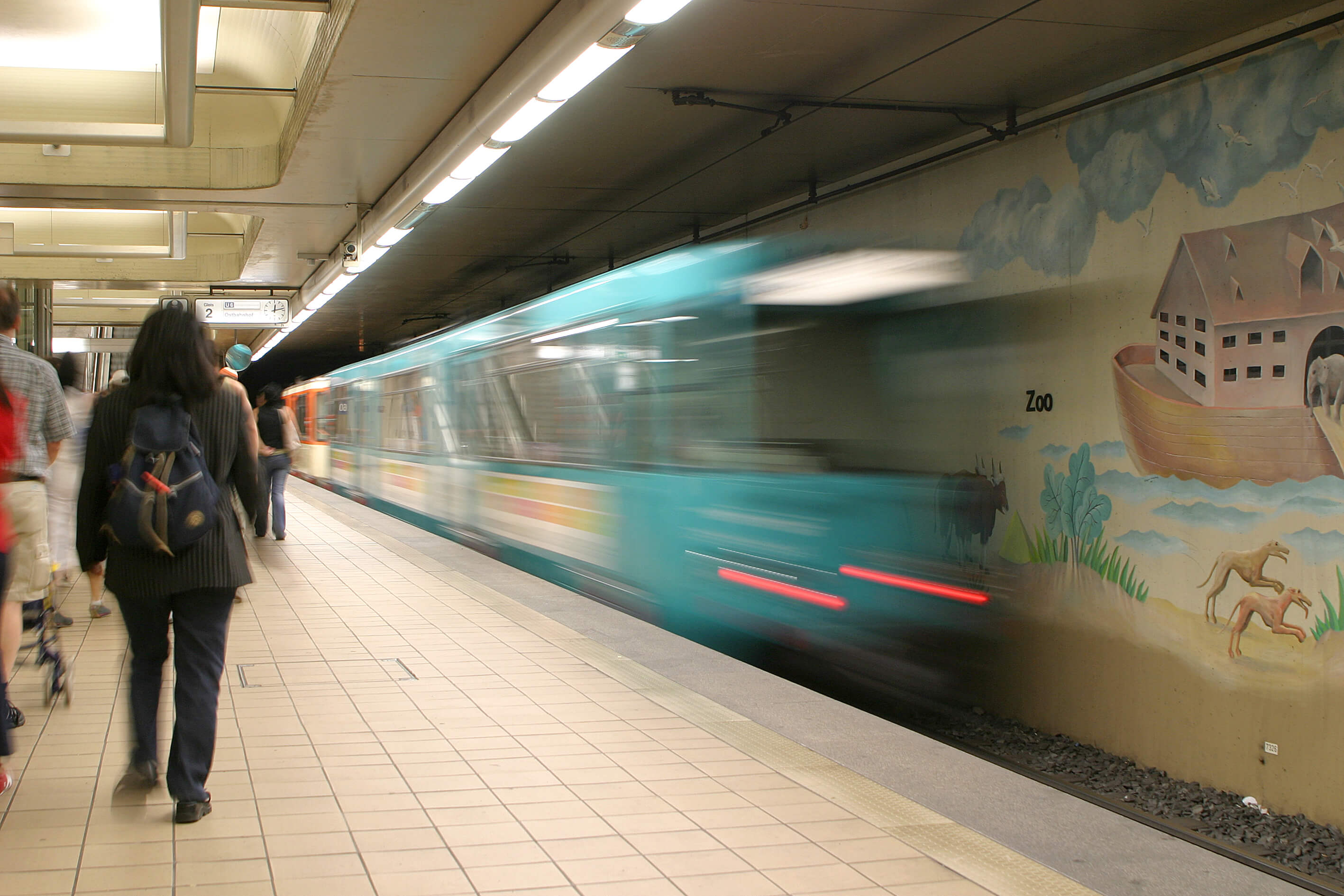 Bahn bei der Einfahrt an der unterirdischen Haltestelle an der Passanten auf dem Bahnsteig laufen.