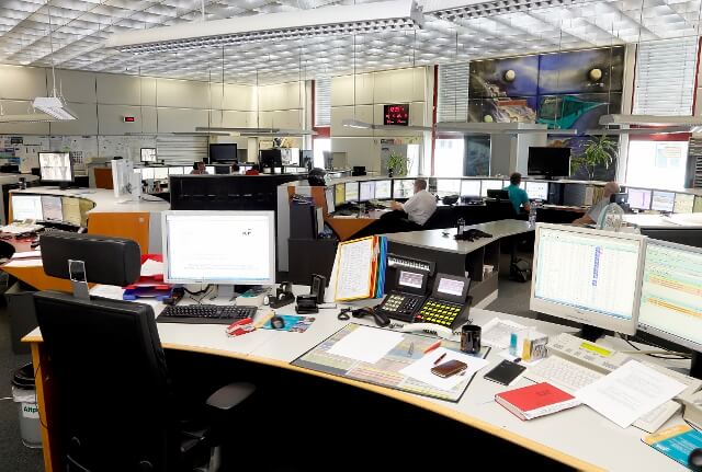 Großraumbüro der Betriebsleitstelle mit vielen Bildschirmen, Telefonen und Unterlagen.