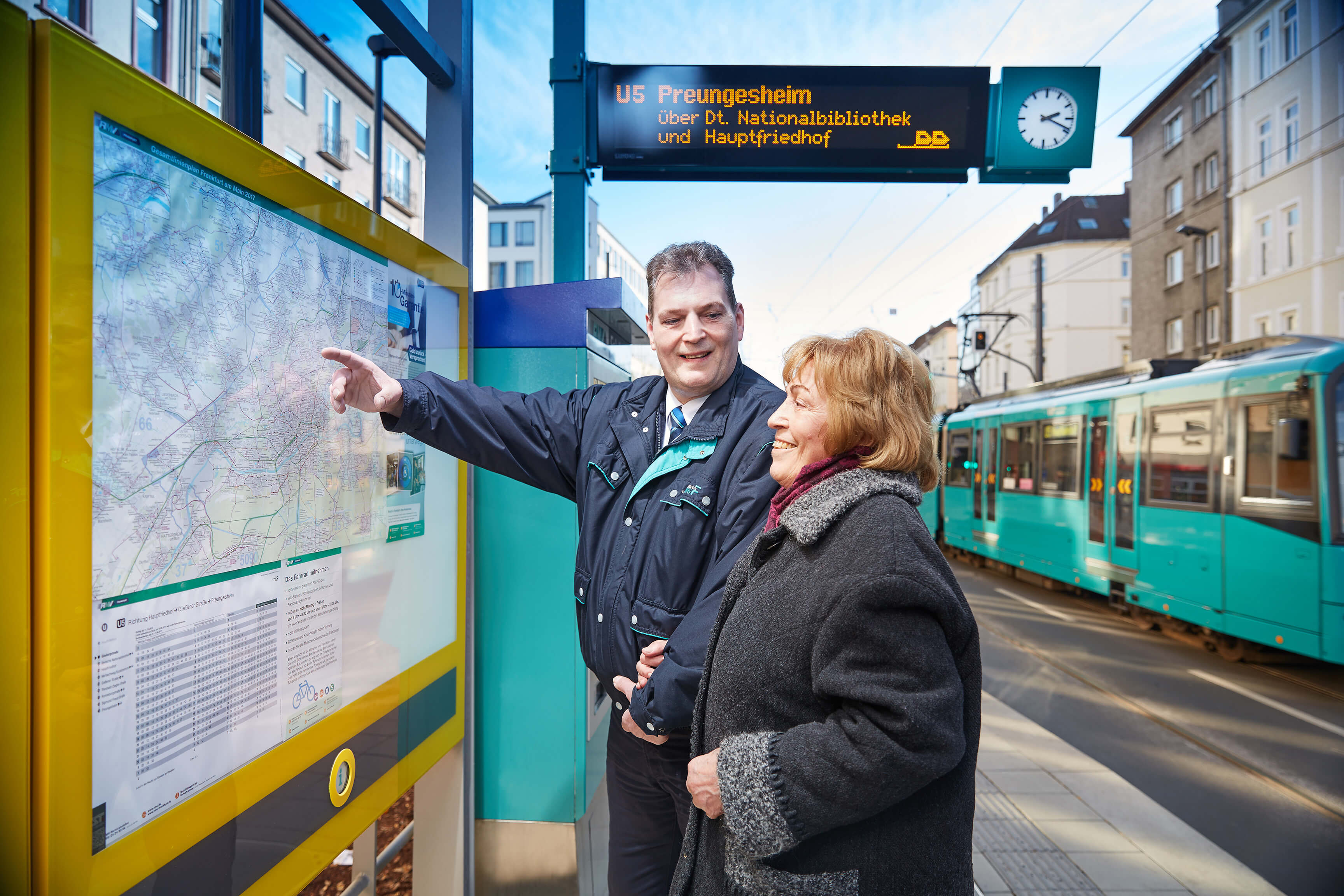 Mitarbeiter der VGF zeigt Dame den Fahrplan-Aushang am Bahnsteig.