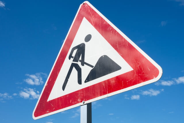 Straßenschild "Bauarbeiten" vor dem fast wolkenlosen Himmel.