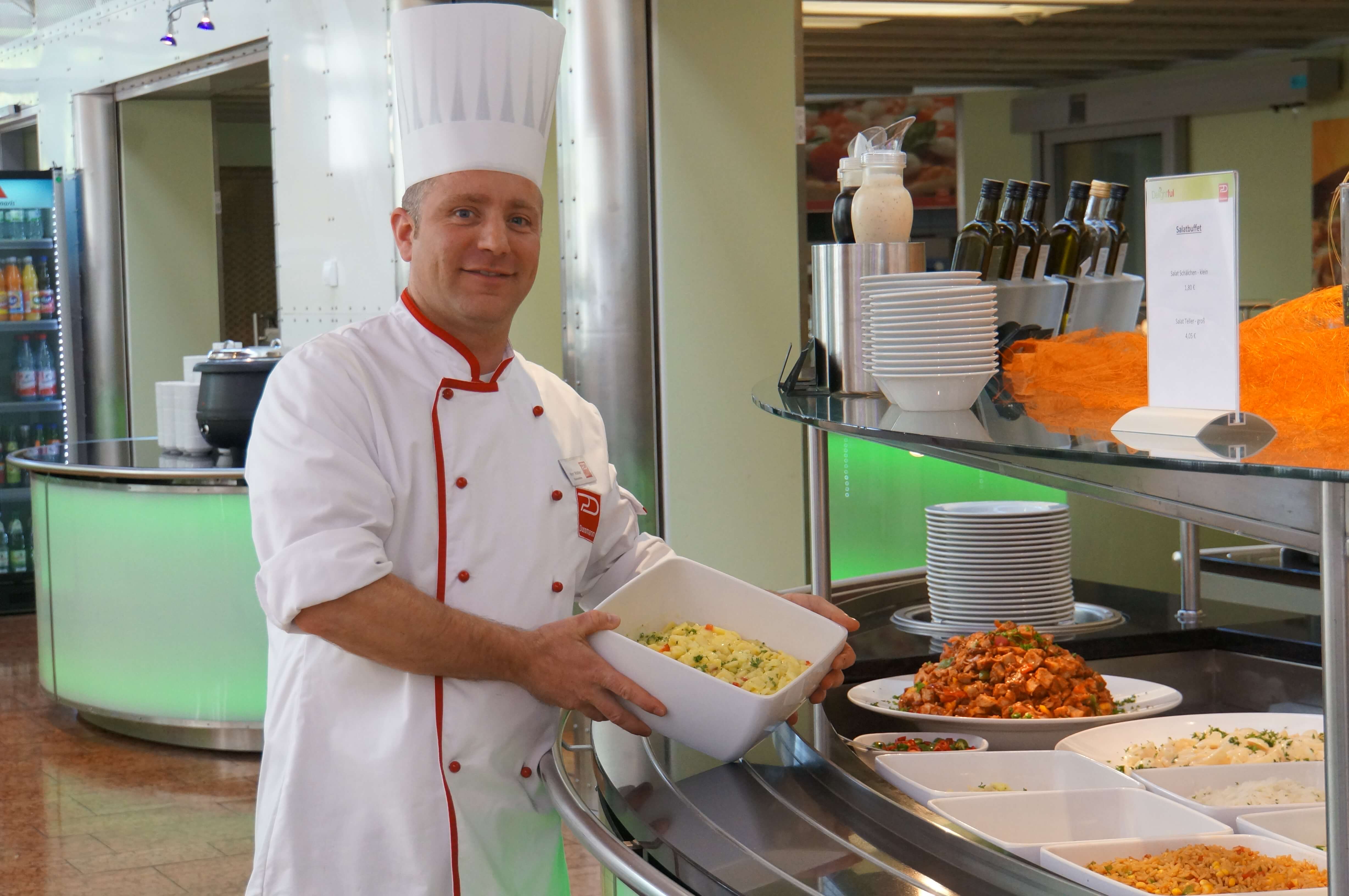 Koch in Arbeitskleidung beim Befüllen der Theke in der Kantine.