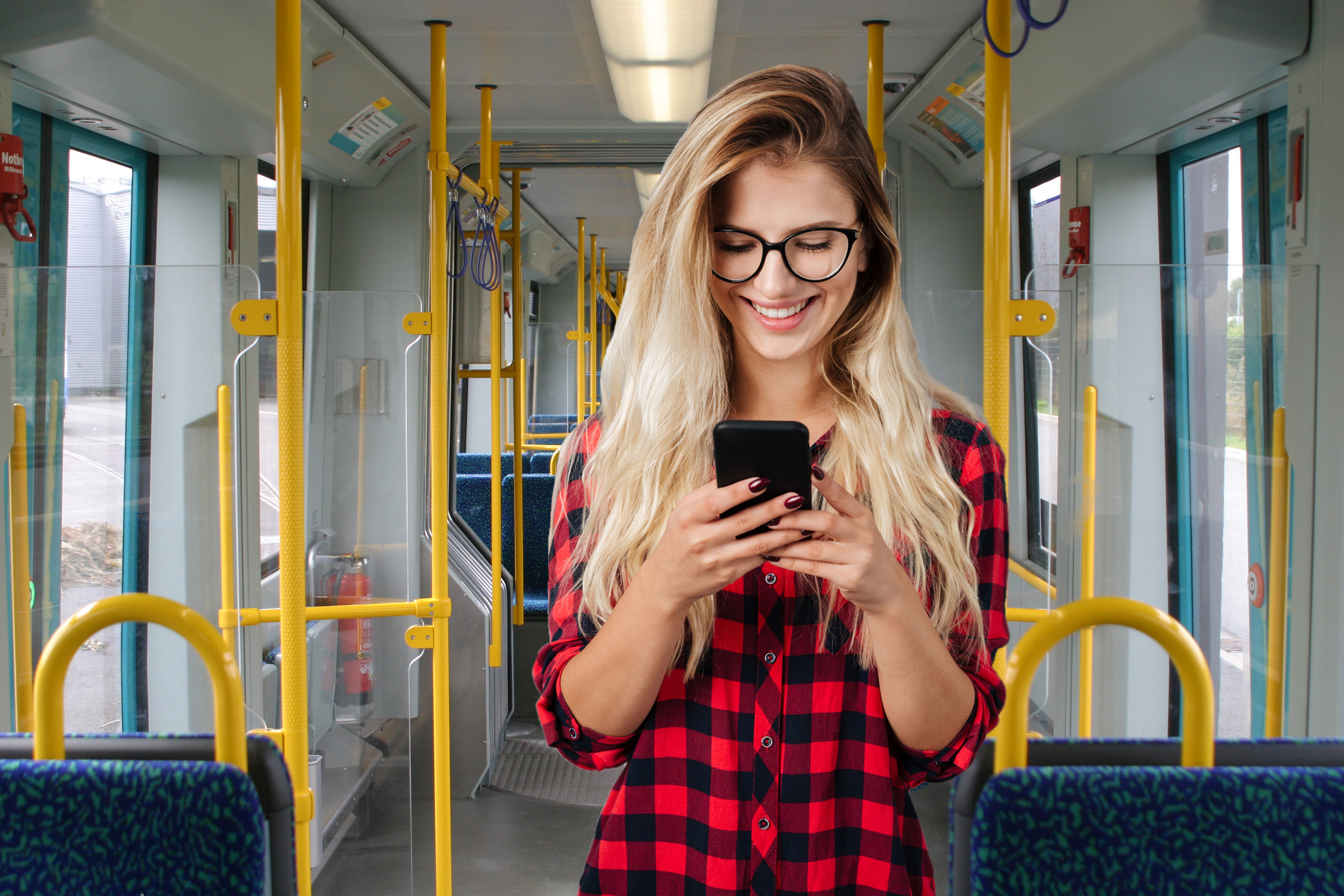 Junge Frau schaut lächelnd auf ihr Handy in der Bahn.
