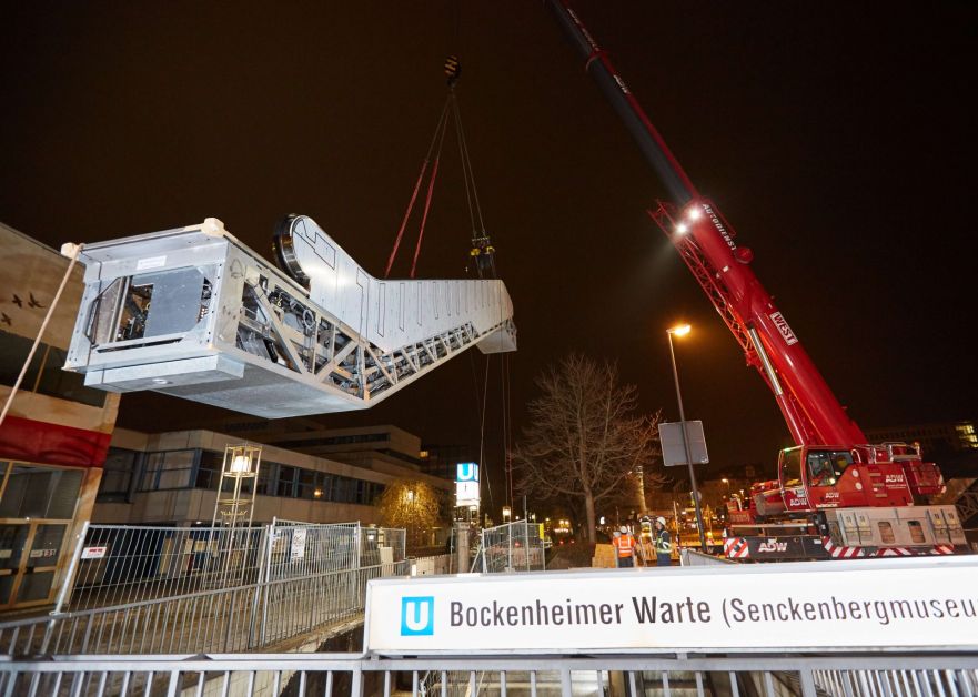 Fahrtreppen-Erneuerung - Kran hebt bei Nacht ein Rolltreppensegment hoch